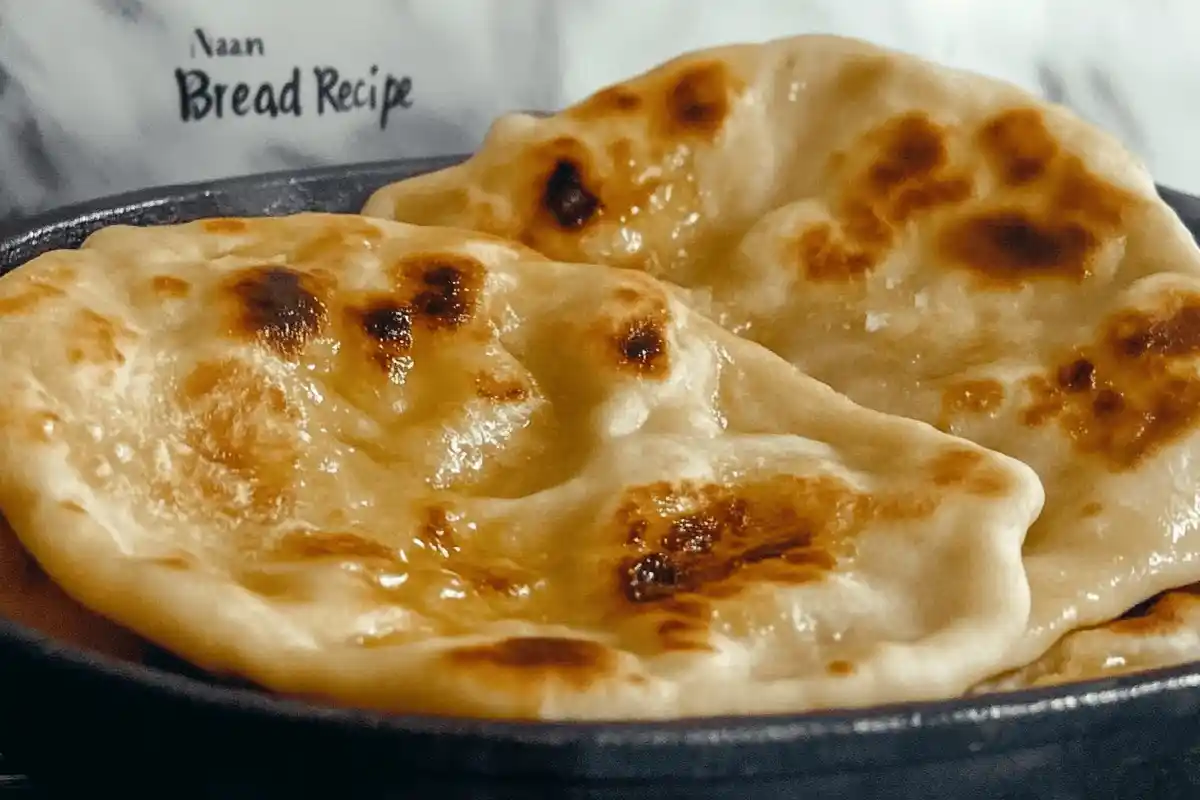 Freshly cooked naan bread brushed with melted butter, served on a wooden platter with a side of garlic cloves and chopped cilantro."