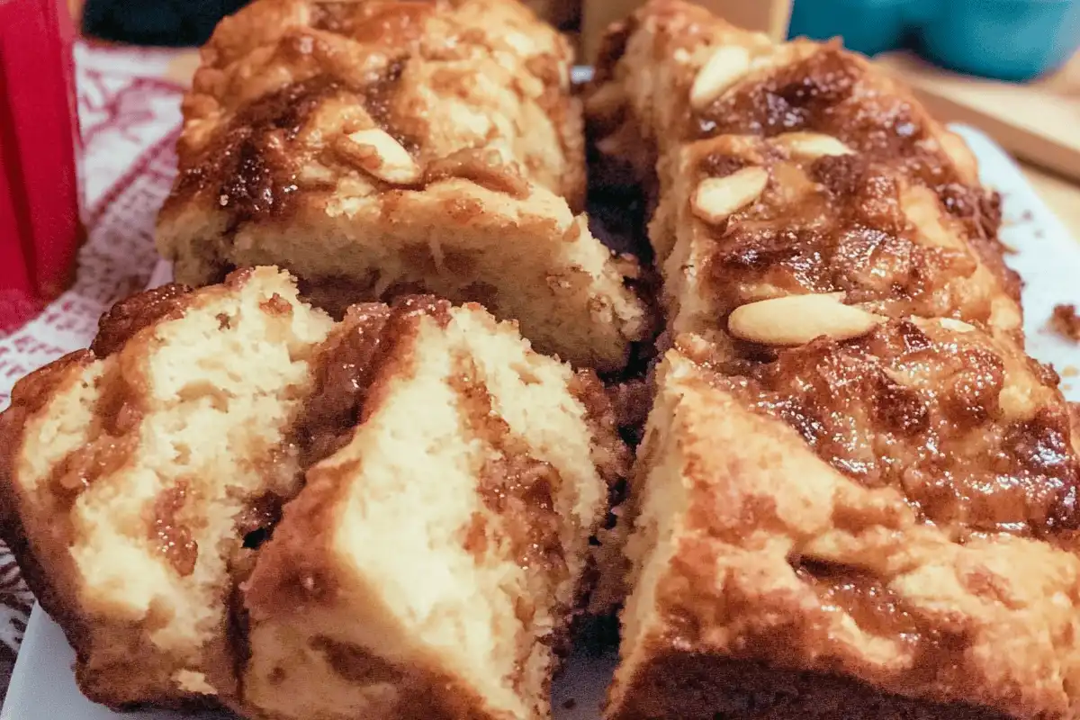 A freshly baked loaf of apple pie bread on a wooden cutting board, dusted with powdered sugar and surrounded by fresh apples and cinnamon sticks