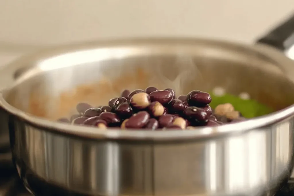 Black beans simmering in a pot on a stove, with some turning purple from cooking.