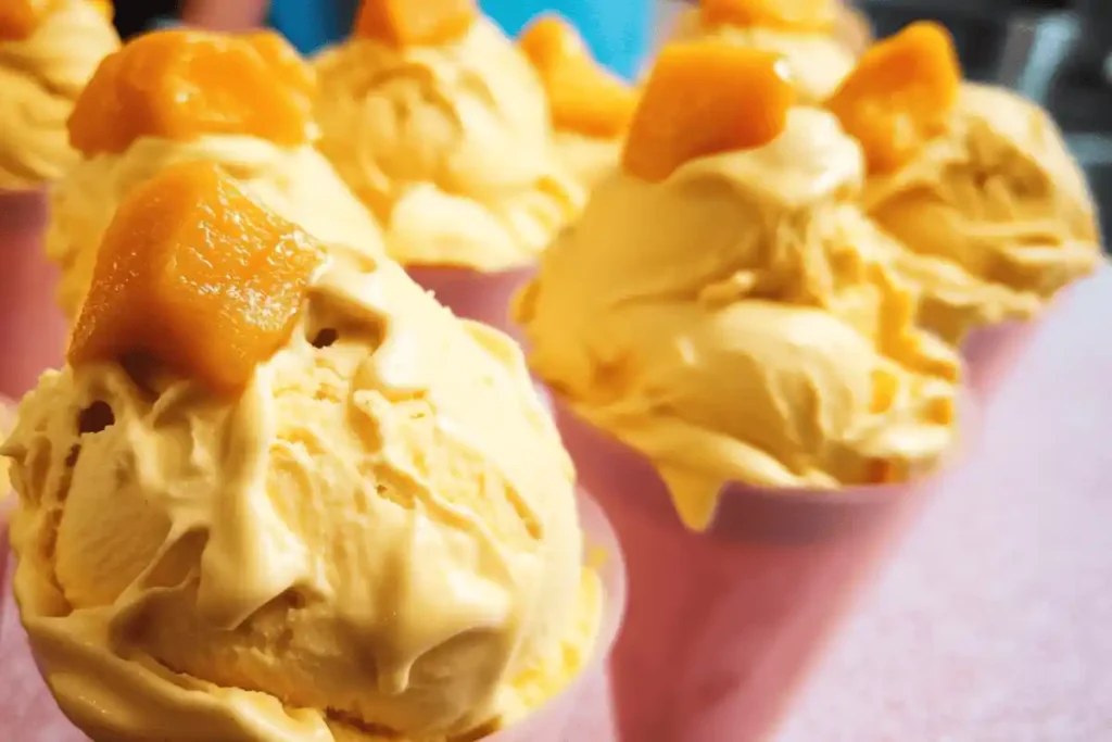 A scoop of mango cheesecake ice cream topped with fresh mango chunks and graham cracker crumbs.